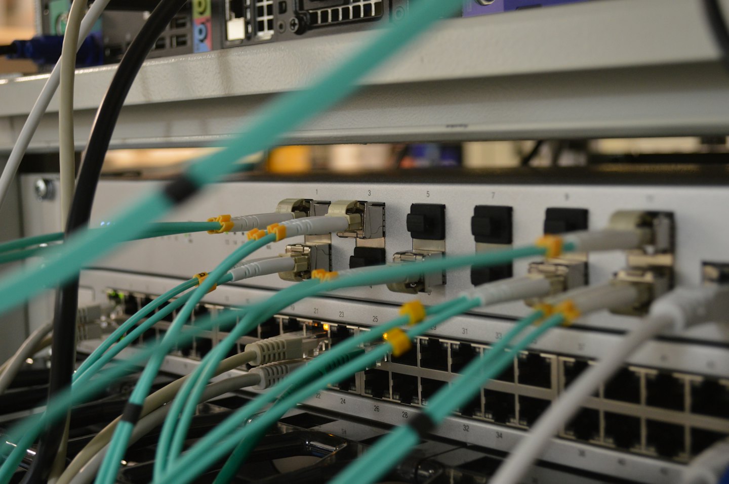 Grey network switch with many teal fiber optic and ethernet cables.