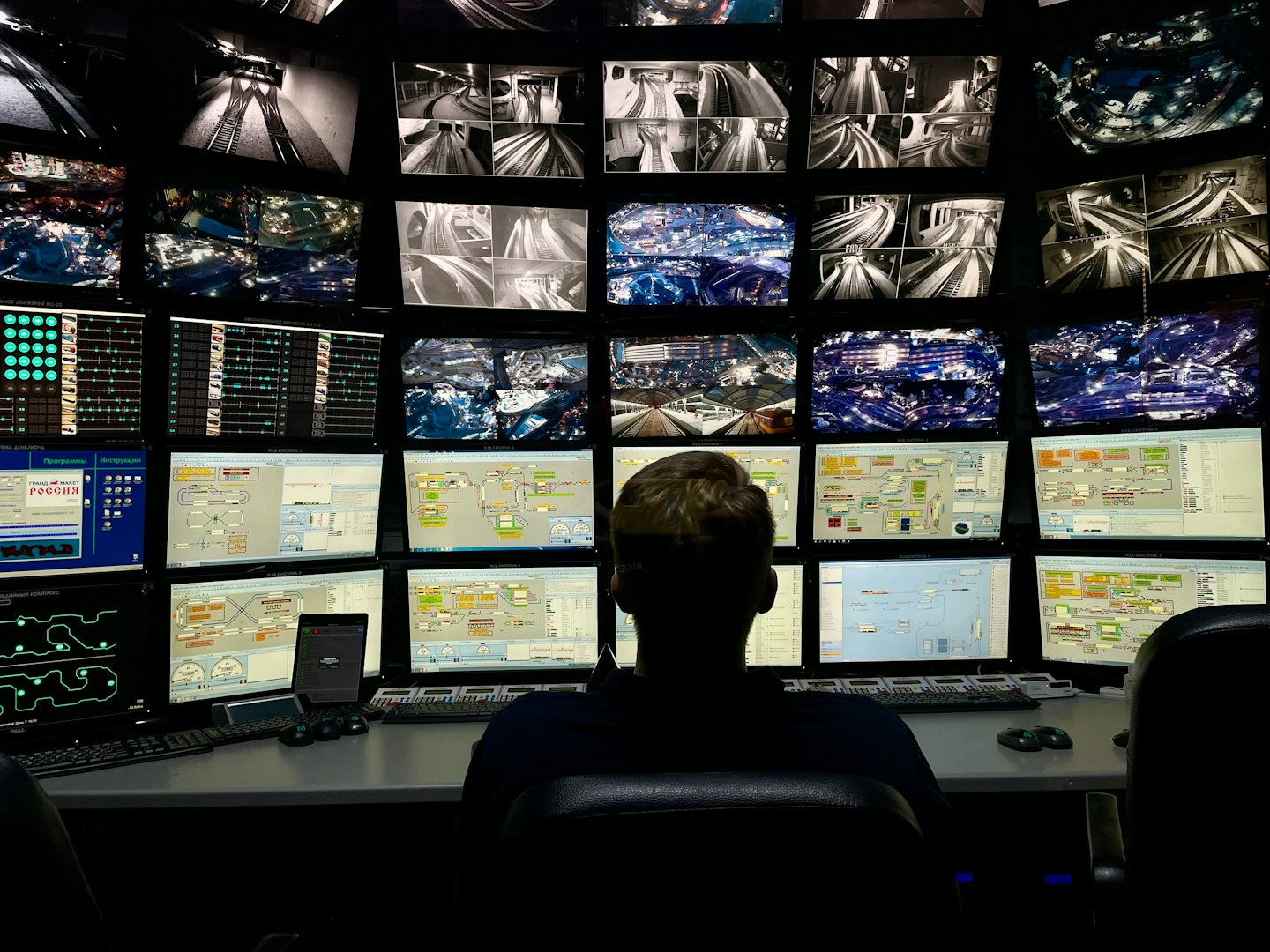 Operator monitoring many computer screens in a dark control room.