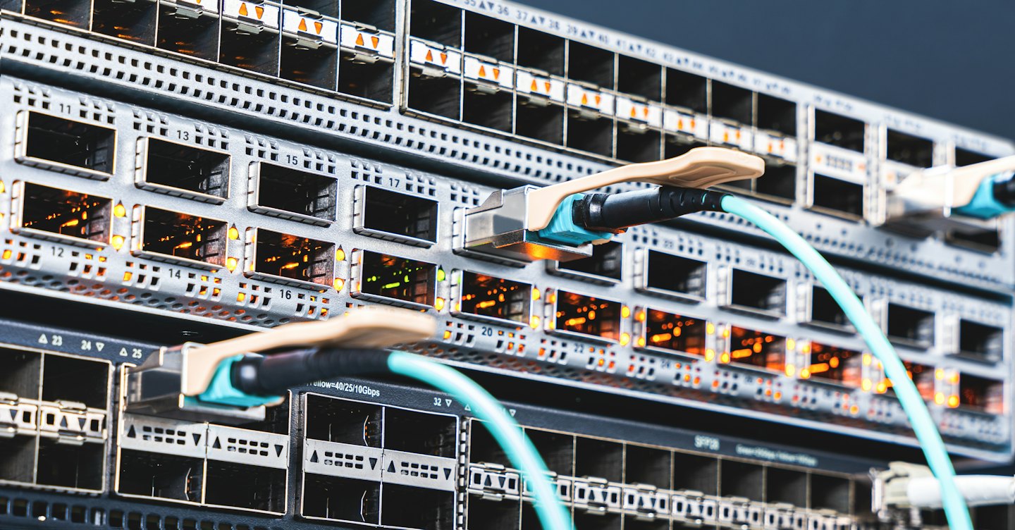 Rows of network switches with fiber optic cables plugged in.